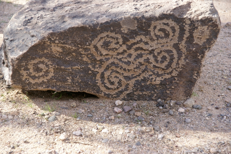 A dark stone sits in the gravelly soil with clear carved markings exposing a lighter color below