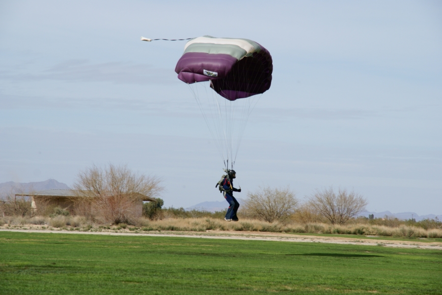 A parachutist glides 6-feet in above the ground below their grey, white, and purple striped parachute