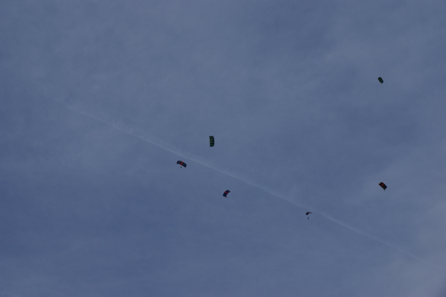 Six parachutes are visible in the sky forming an arch as they float to the ground