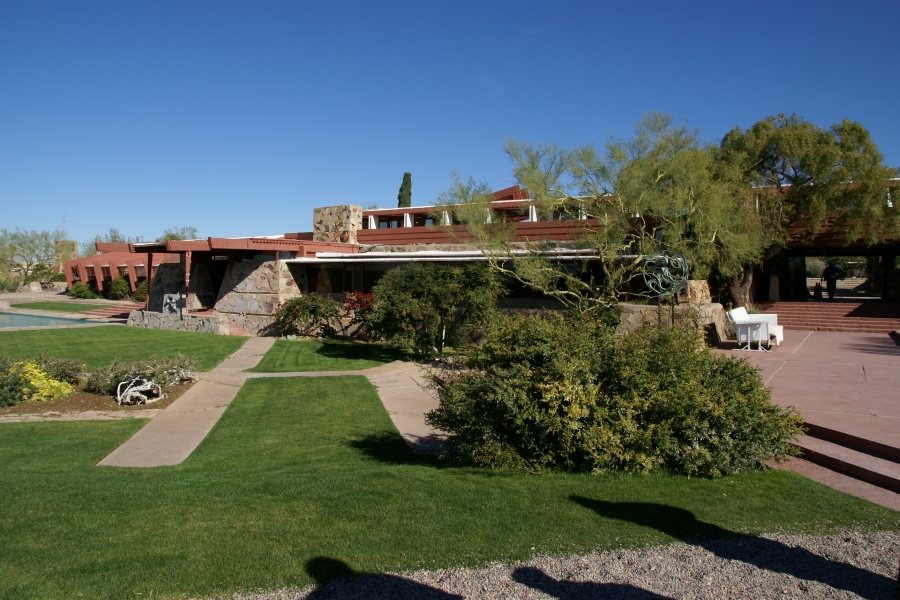 Blue sky of green crass and scrubby trees that grow around and hide the sprawling form of a stone and wood framed building