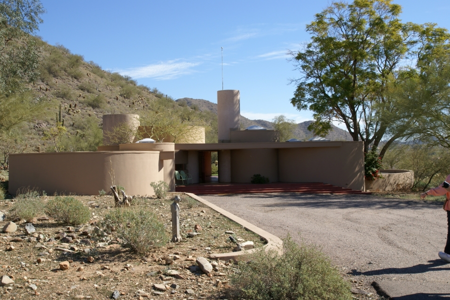 A low tan building made predominately of cylindrical shapes of varying height and diameter sits just below a hillside