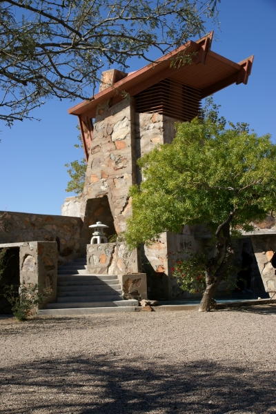 Stairs go up to a stone and concrete tower element with a sloped temper shed roof and louver