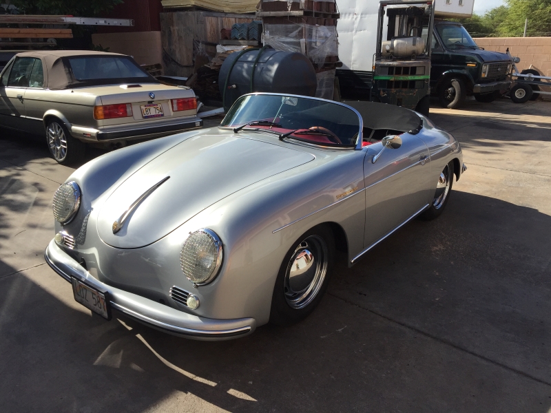 A sleek, silver Porsche Speedster parked in a driveway. Its classic curves and chrome details gleam in the sunlight. The car's open top, red interior, and sporty design evoke a sense of freedom and adventure.