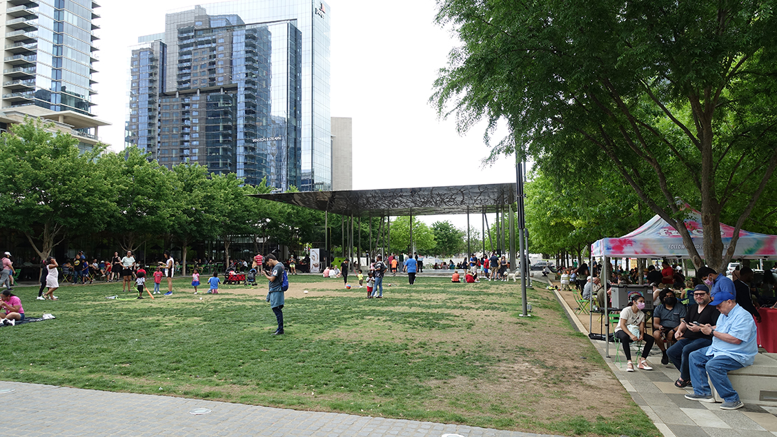 A green space lined by trees in the middle of high-rise glass and steel buildings