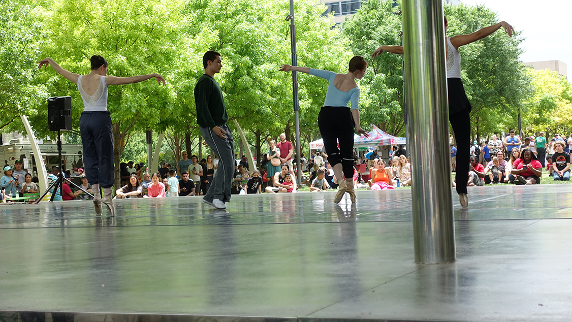Dancers in warm-up pants practice ballet under a shelter