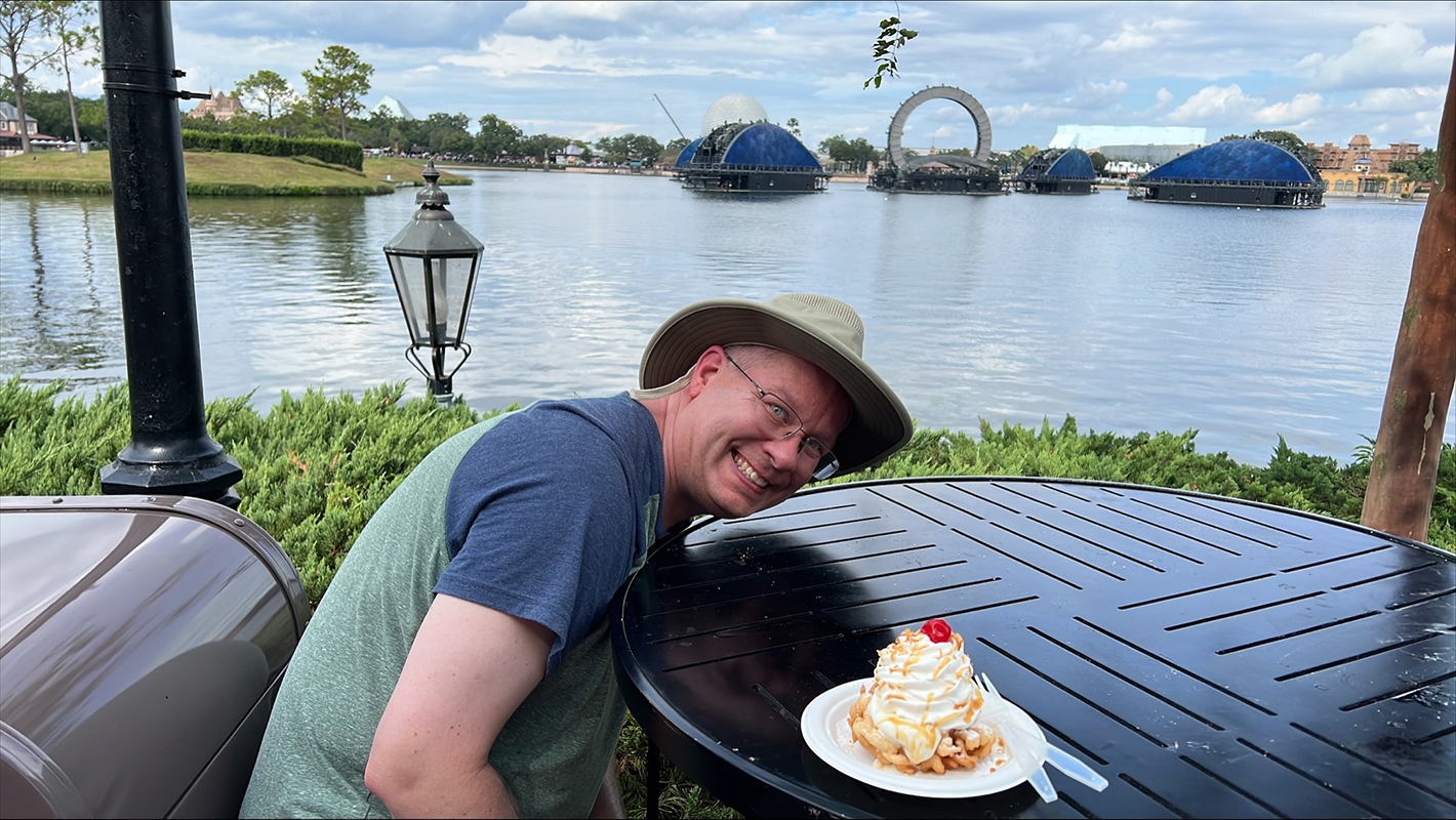 James at EPCOT with a funnel cake on the table ready to be eaten