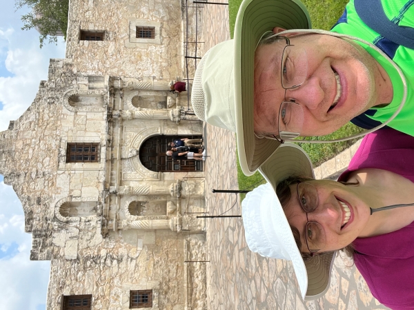 Julie and James standind in front of a wite stone mission style building