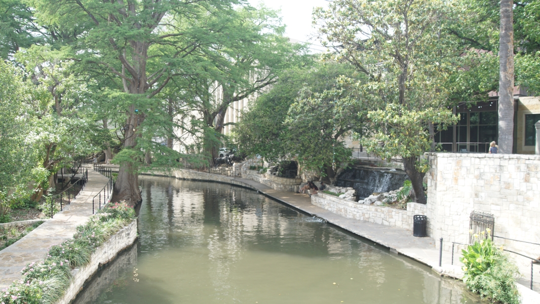 A canal runs between curving stone walkways with fountains and trees on each side