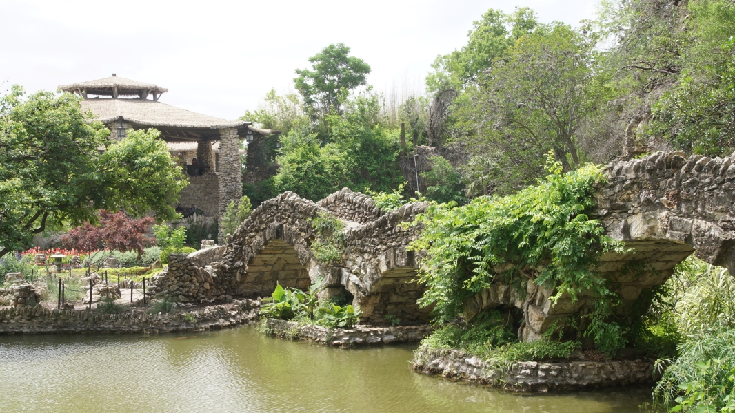 A stone bridge with three arches leads to a flower covered island with a white stone pavilion on the hill behind