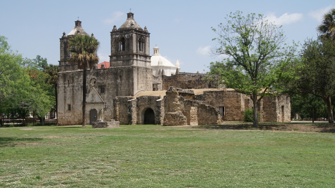 A white stone church with two towers with remnants of stone buildings connected to one side