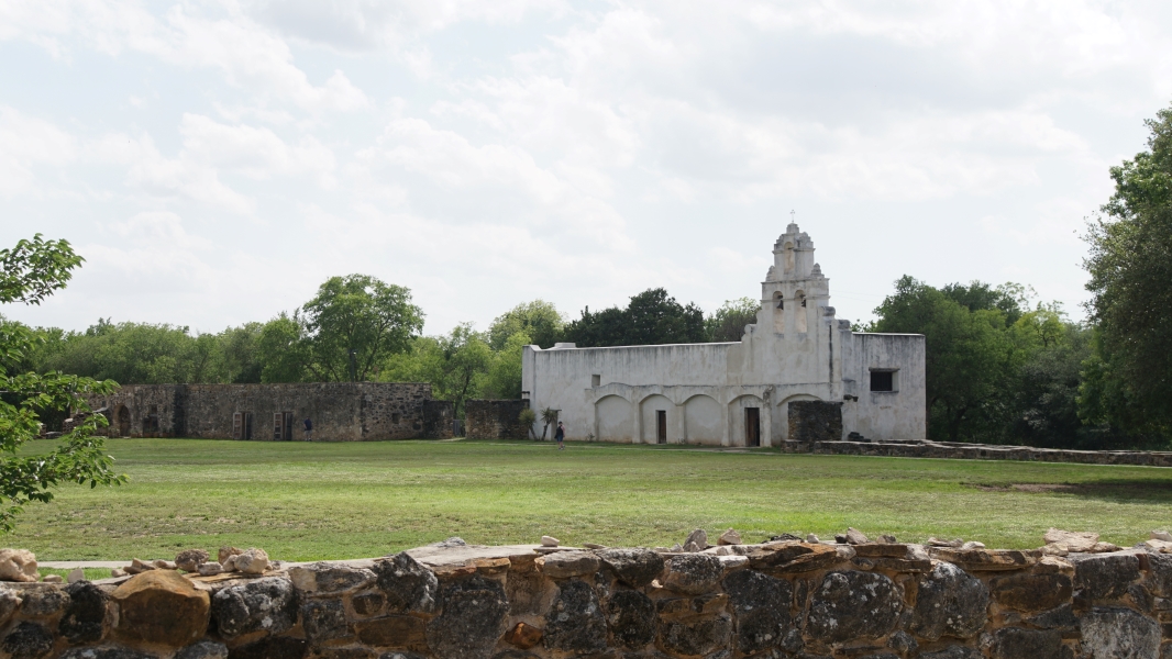 A small, whitewashed church sits beyond a field of wild-flowers and grass