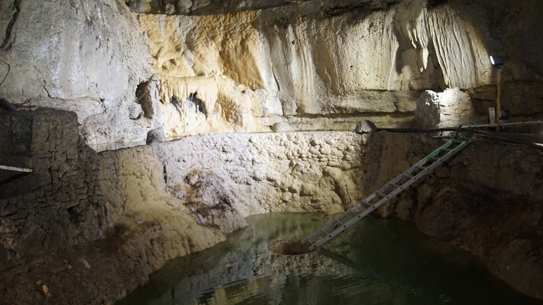 A ladder extends to a hole where water in a cave drops into a lower cavern