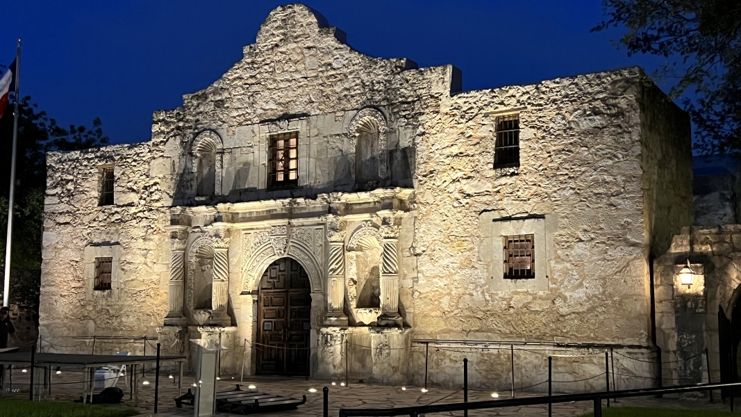 A white stone building with traditional Hispanic mission style lit by bright up lights