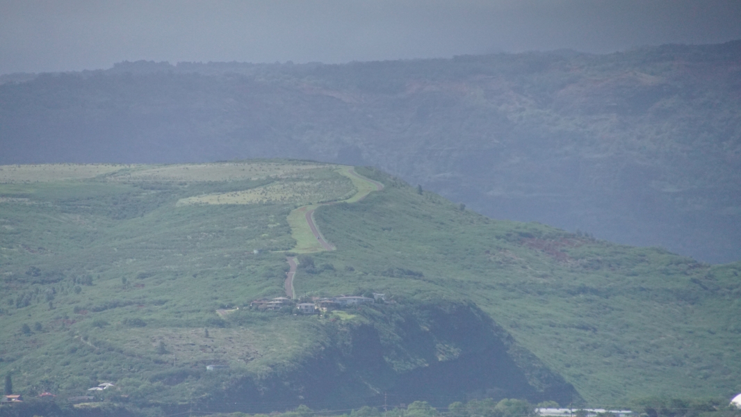 A narrow blank strip of road winds up the side of a hill above two- and three-story structures situated on a cliff