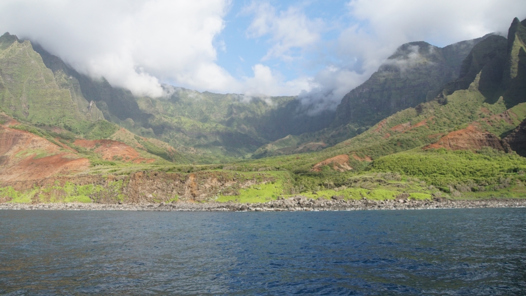 Green covered canyon walls creating a deep arched valley extending away from the water with clouds starting to form near the top