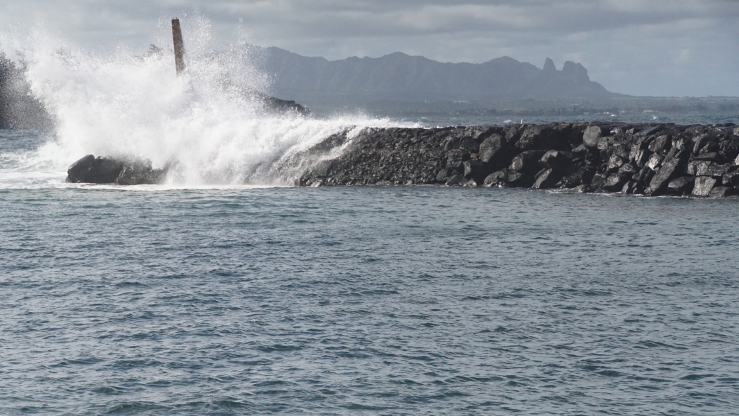 What sprays into the air and runs over a stone embankment as a wave crashes into a breakwater built to create a calm bay