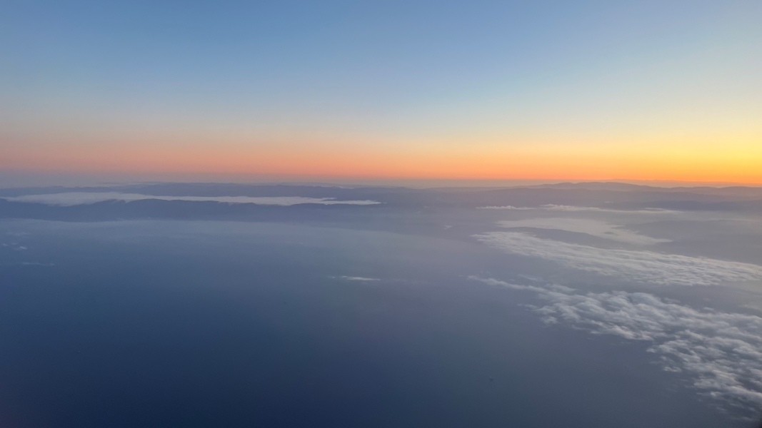 Red and yellow streaks blend into blue skies above broken clouds above the ocean and dark hills
