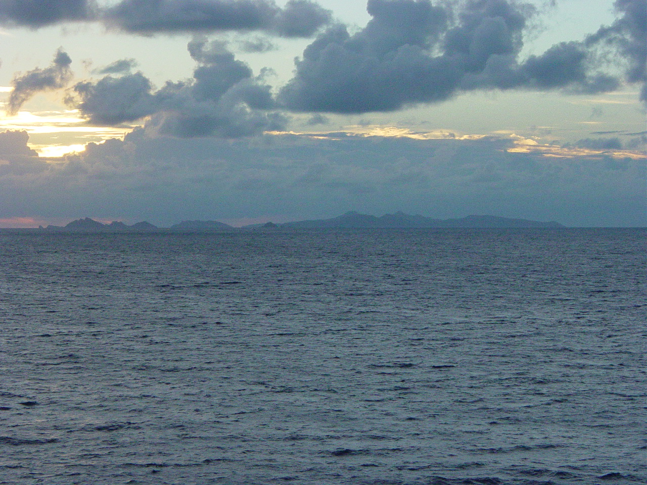 Sunrise behind clouds with an island visible in the distance