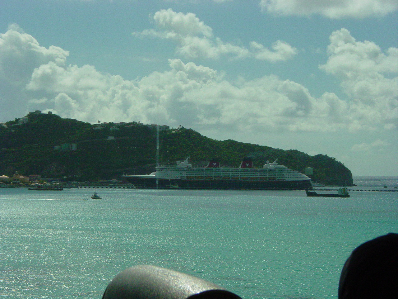 Disney cruise ship docked with green hill beyond