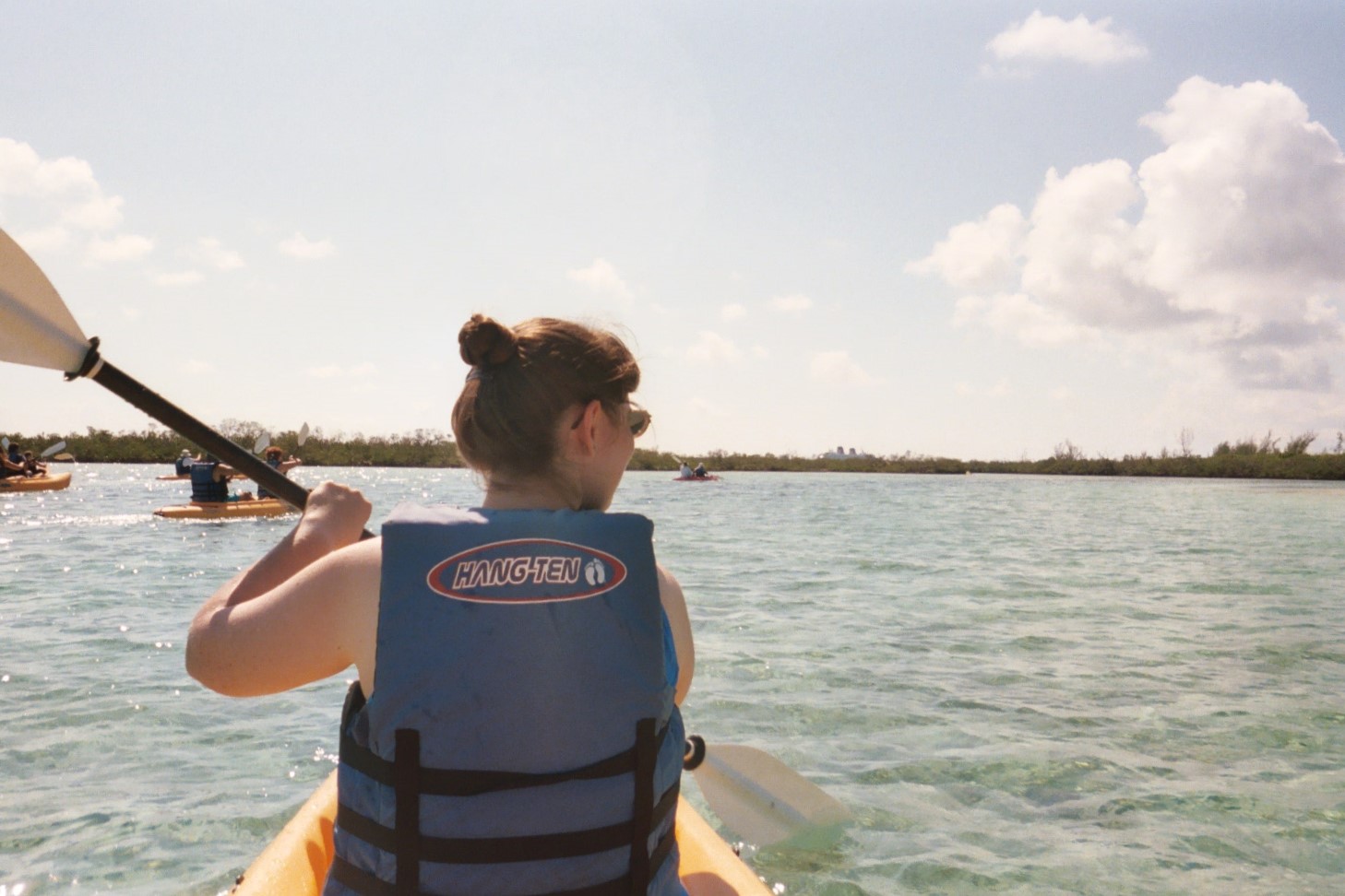 Julie paddling through water with kayakers and scrub brush beyond