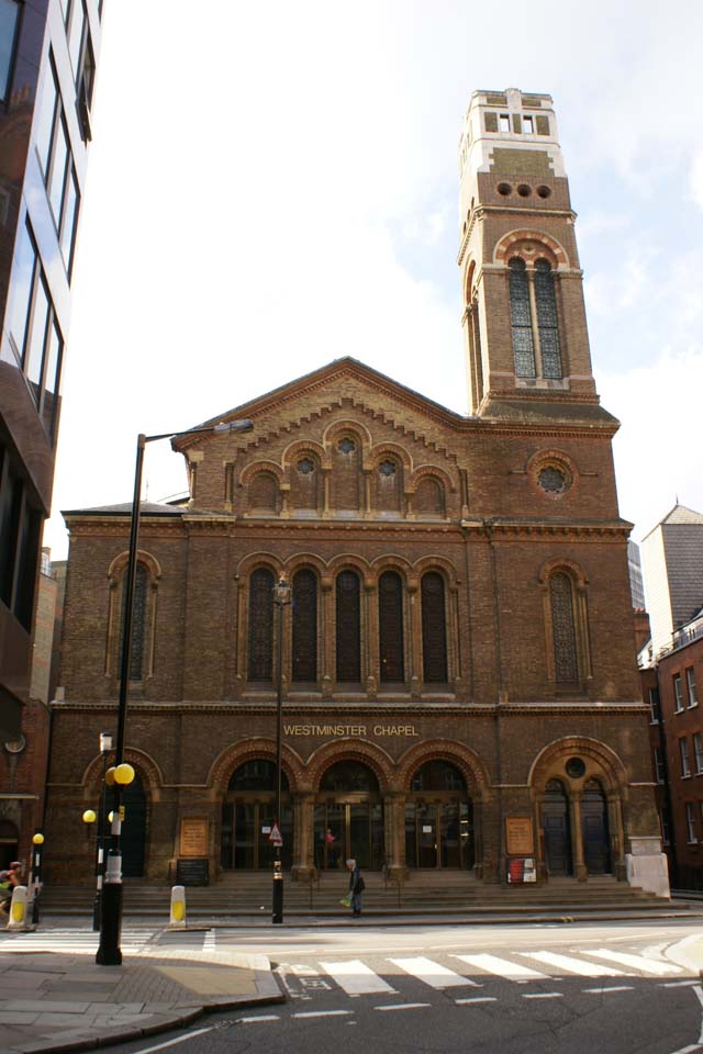 Red brick church with single bell tower between other buildings