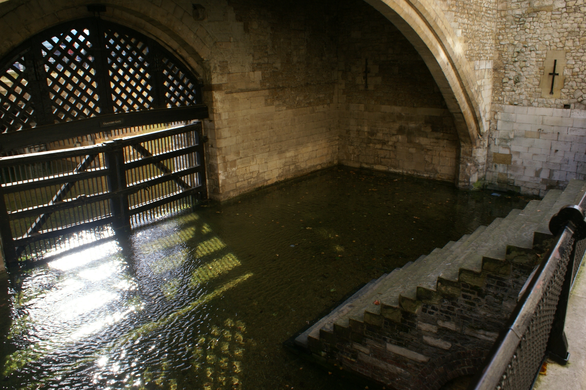 Stone stairs down to a stone arch with a gate over a pool of dirty green water