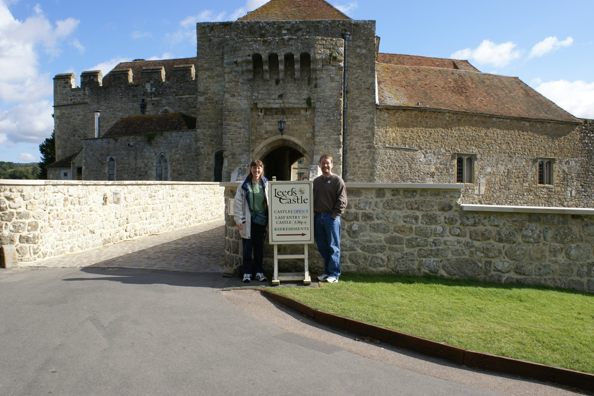 Julie and James stand by a sign in front of a round stone tower with a gate