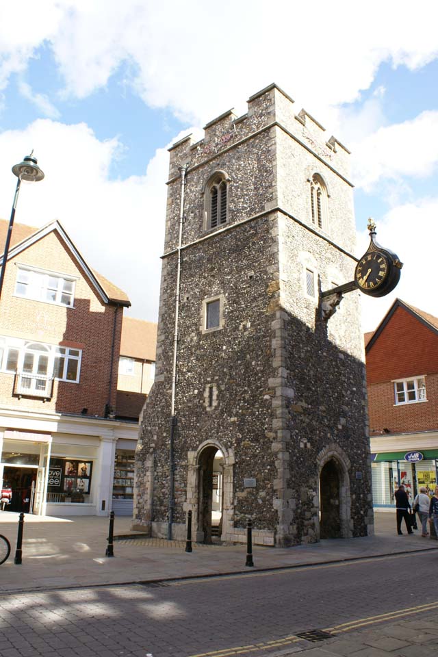 Crenellated three-story gray stone tower with clock hanging of one side