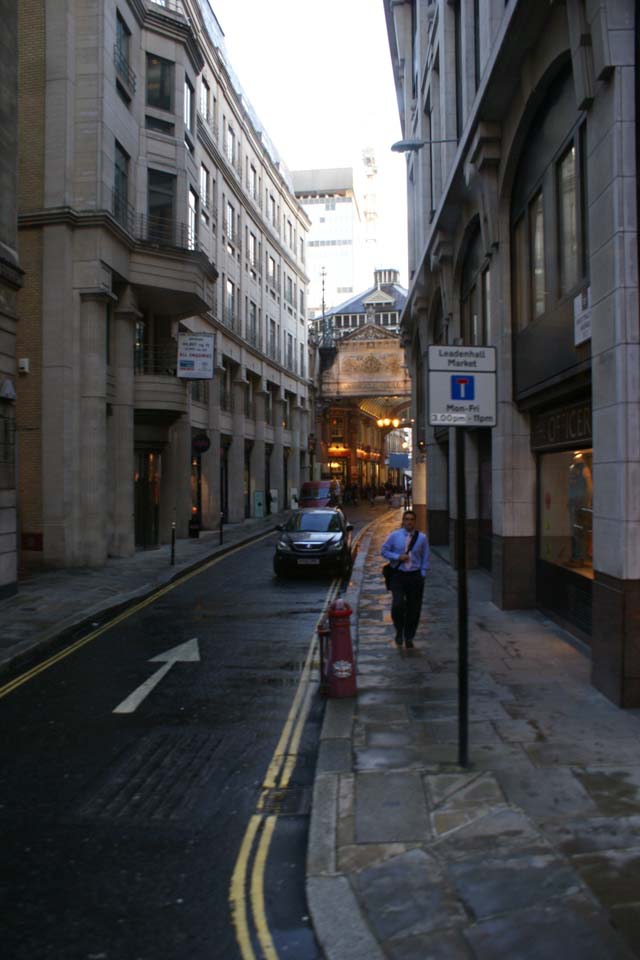 Narrow street between tall buildings passes below a building on an arched bridge