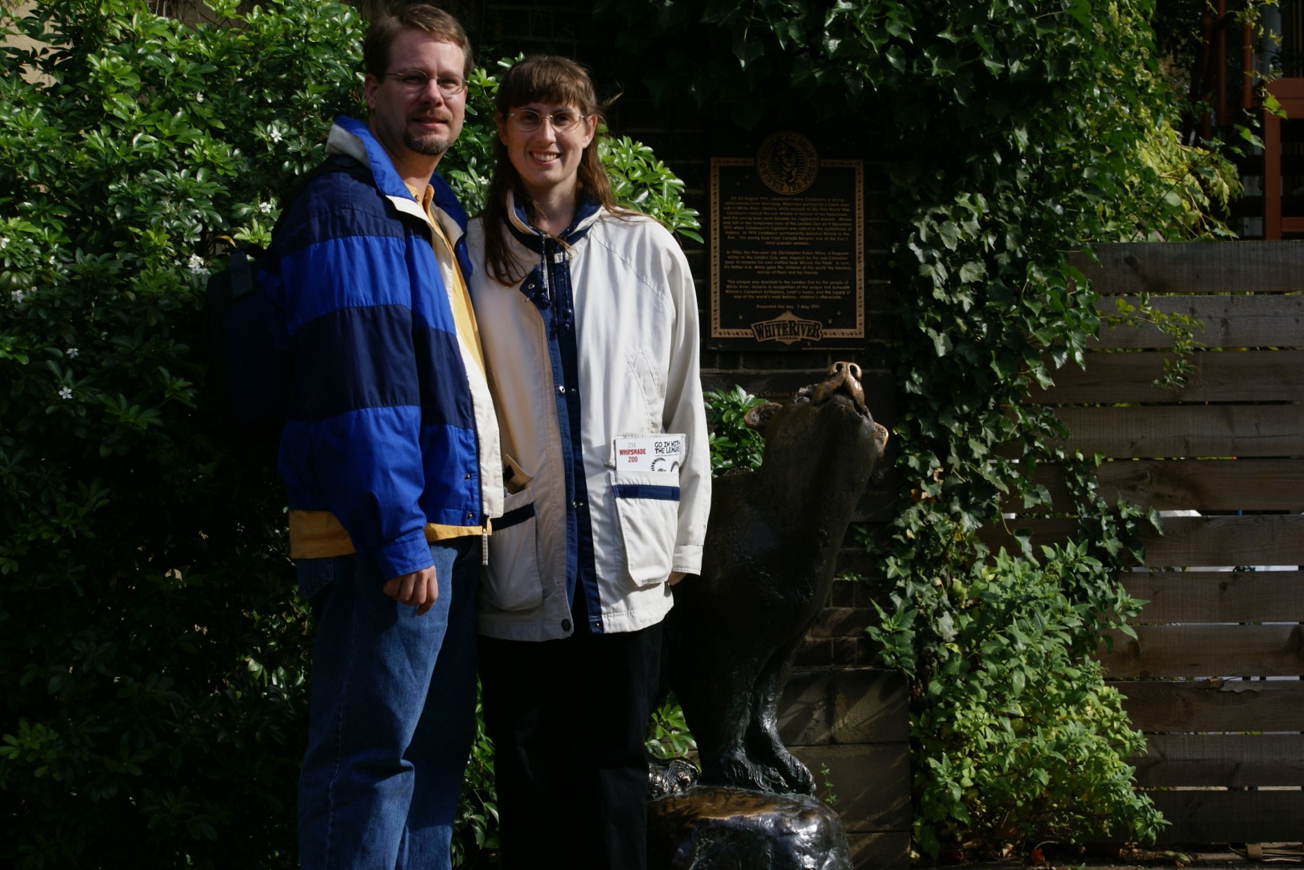 James and Julie pose next a statue of a small bear in front of a plaque
