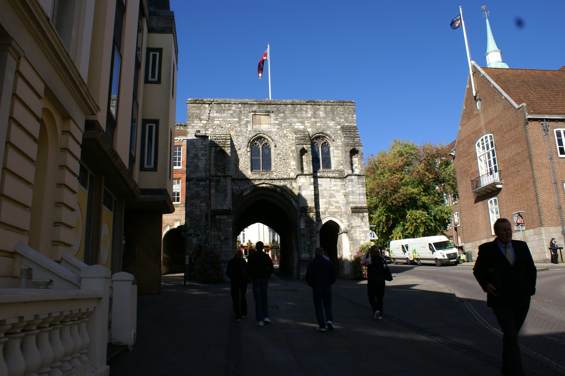 A section of a gray stone wall with a large arch stands alone amongst more modern brick and stucco buildings