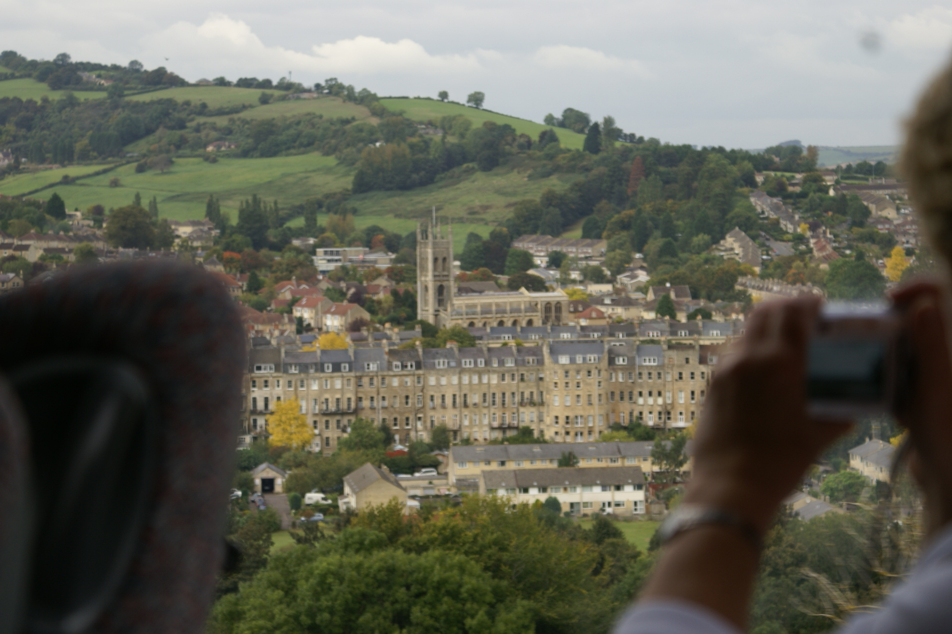 Tan buildings include a large abbey stand in the valley between green hills