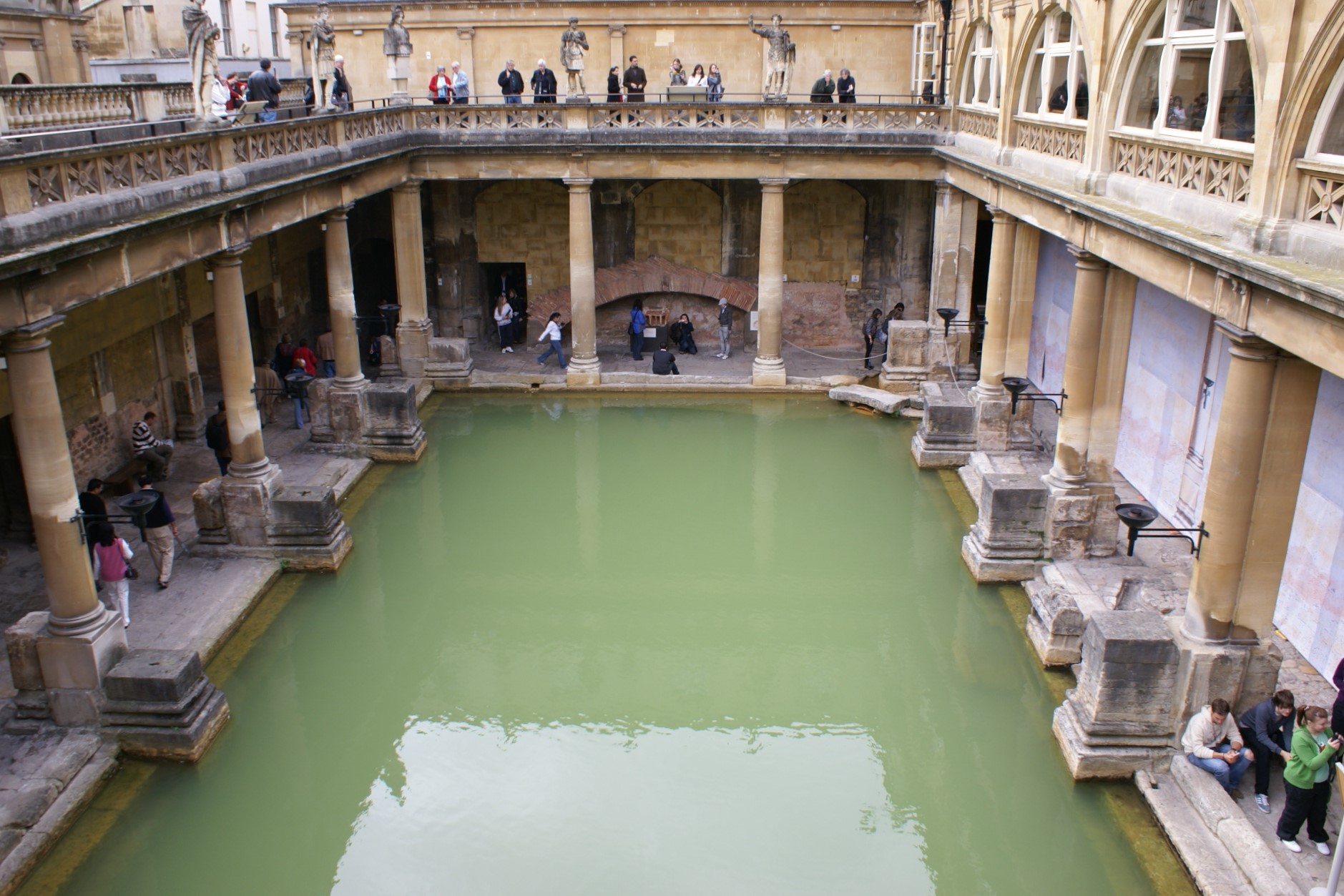 A pool of green water stands surrounded by ionic columns holding up an upper-level walkway