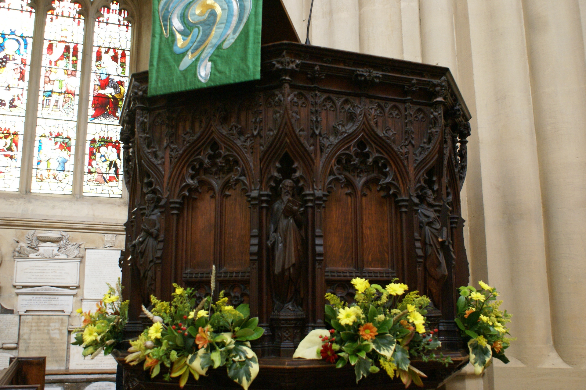 Ornately carved wood platform against a white column surrounded by flowers
