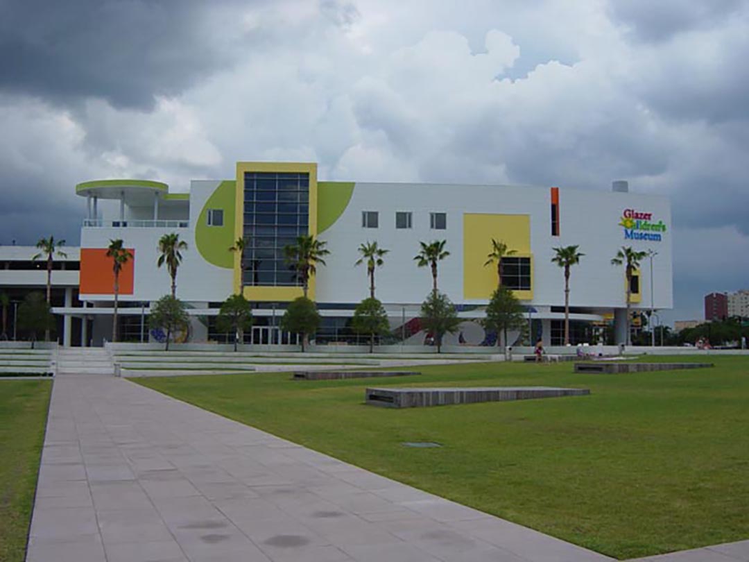 A three-story white walled building with patches of bright green and yellow rises above a urban park