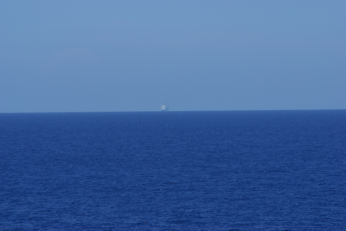 A cruise ship on the horizon between the dark blue sea and light blue skies