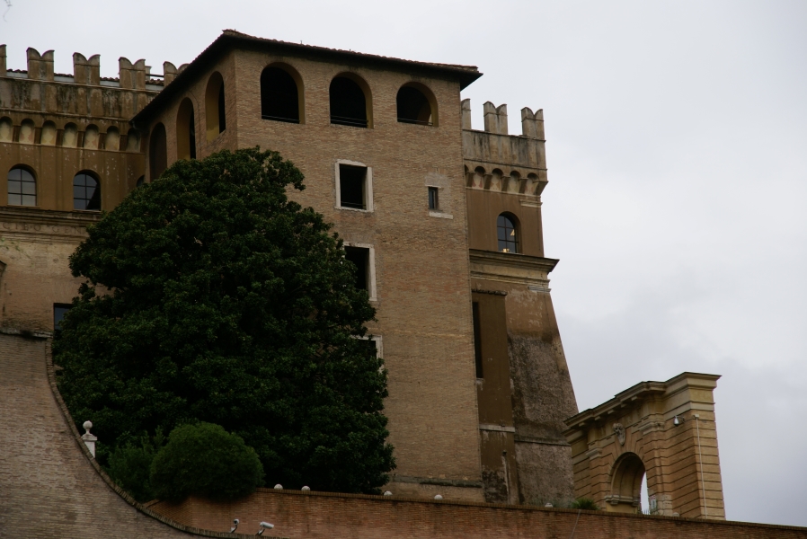 A square brick tower extends from the walls of a large fortification with sloped walls and crenellations the appear to have open books on top