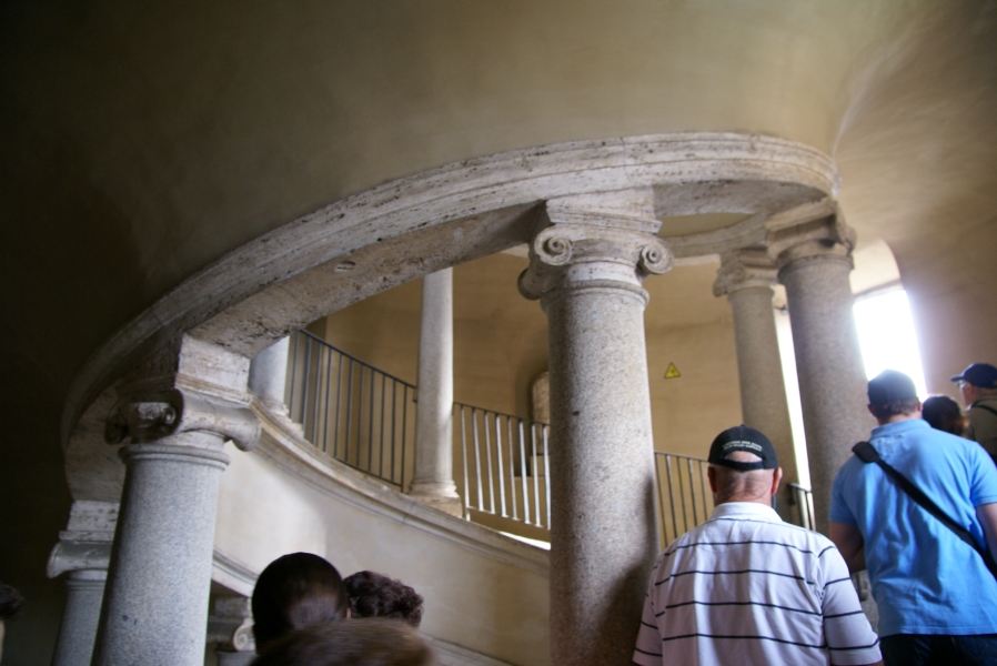 Black railings fill the gaps between white marble columns with doric capitals that form the interior of a spiral ramp