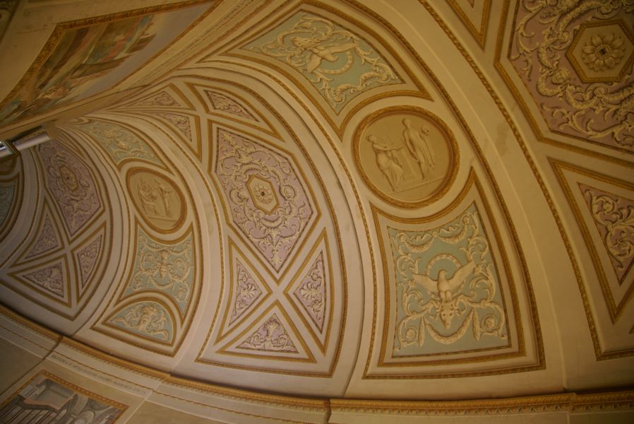 Ornately painted ceilings with blue and lavender backgrounds give the illusion of carved stone work as an arched ceiling wraps around a curve