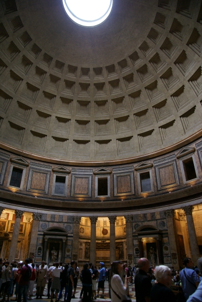 Gray stone of decreasing inset squares create a dome that has a circular opening at the cap are held aloft by ornate brown, pink, and white stone carved walls and colonnades
