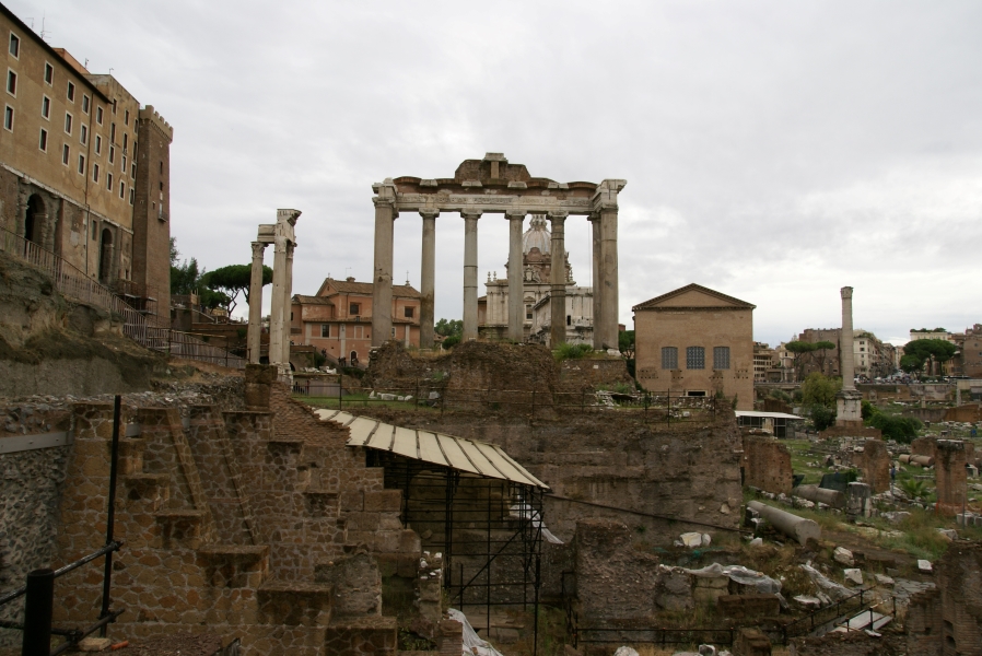 Black scaffolding supports a wood canopy covering a section of ruins under excavation with 30-foot-tall white marble columns supporting the remains of stone bands