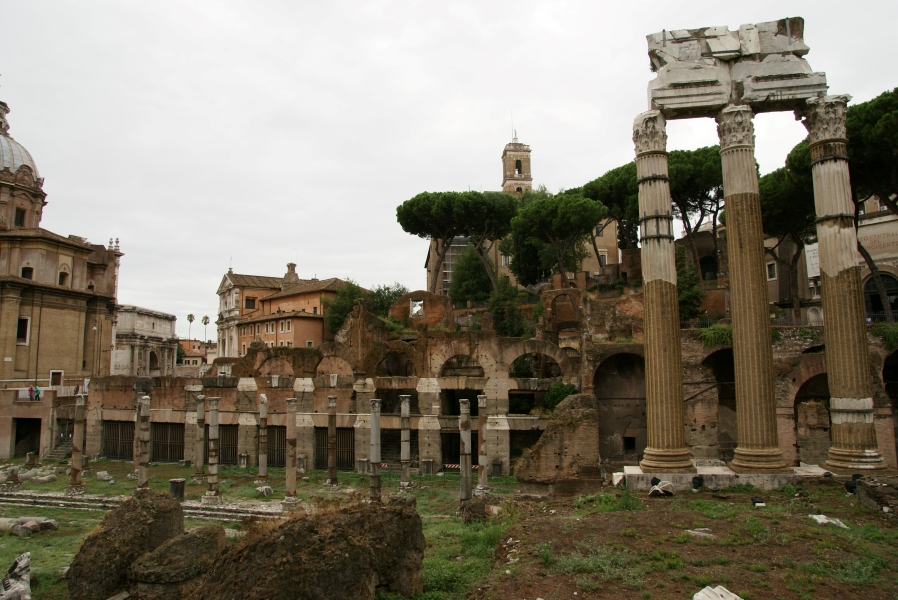 Excavations with arches and walls built into a hillside with free standing columns in front of more recent stone buildings