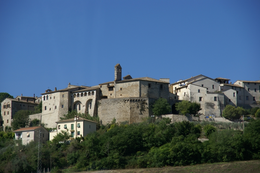 Old stone walls support houses built on the side of a hill with newer construction amongst green trees at their base