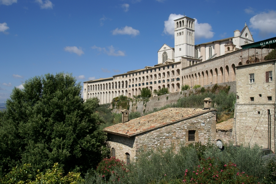 White stone walls with arches stand above a hill surrounding a white church with a square bell tower