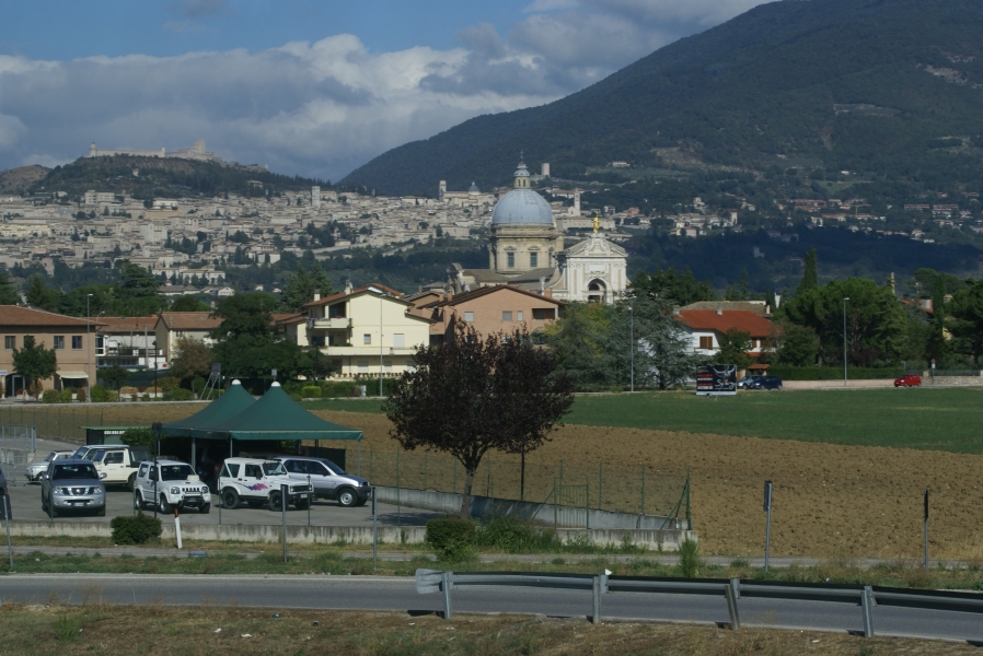 A large complex sits atop a hill with a larger city on the slopes leading up while in the valley below stands a church with a gray dome and bright white entry facade