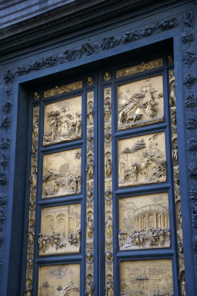 A black frame surrounds doors made of highly detailed bronze panels each depicting a scene from the life of Christ