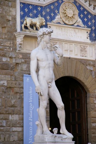 A white marble statue of a nude man stands before the entrance to a building