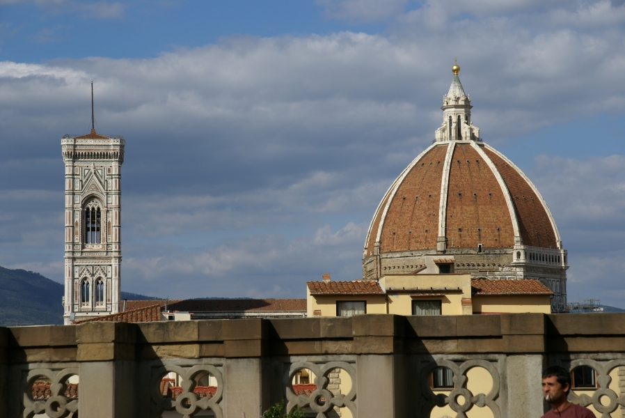 A white bell tower with mosaic detailing and a white ribbed dome with red tiles extend above the roofs of Florence