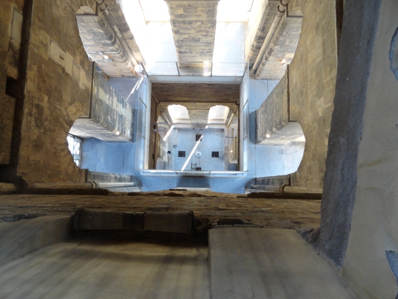 Looking almost straight down to a landing 20 feet below and then the ground another 20 feet beyond with tall pointed arched openings in the walls allowing light into the center of the bell tower