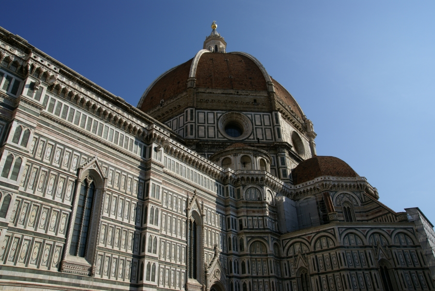 White, green, and pink stone tiles form regular pattens around windows on the side and chapel walls around the dome of the Florence Cathedral
